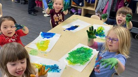 Kids sitting at table finger painting with yellow and blue paint